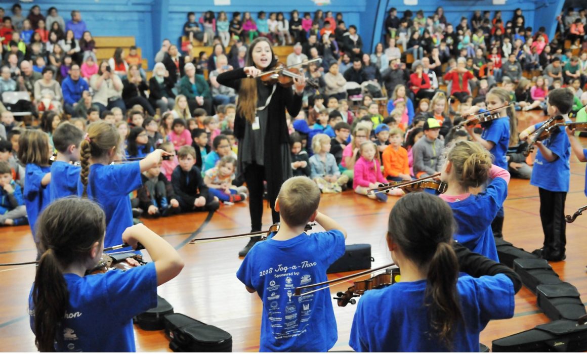 Student musicians and their instructors playing violins at assembly