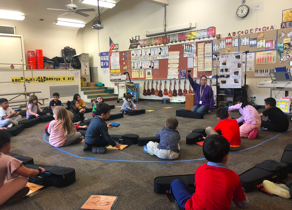 Teacher on the floor of the music room with children sitting around them