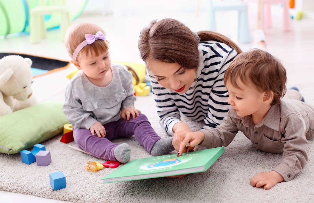 Woman lying on the floor reading a book to a baby and toddler